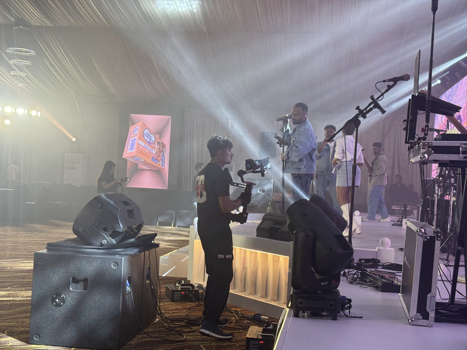 Gimbal operator filming a performer on stage with a graphic screen behind